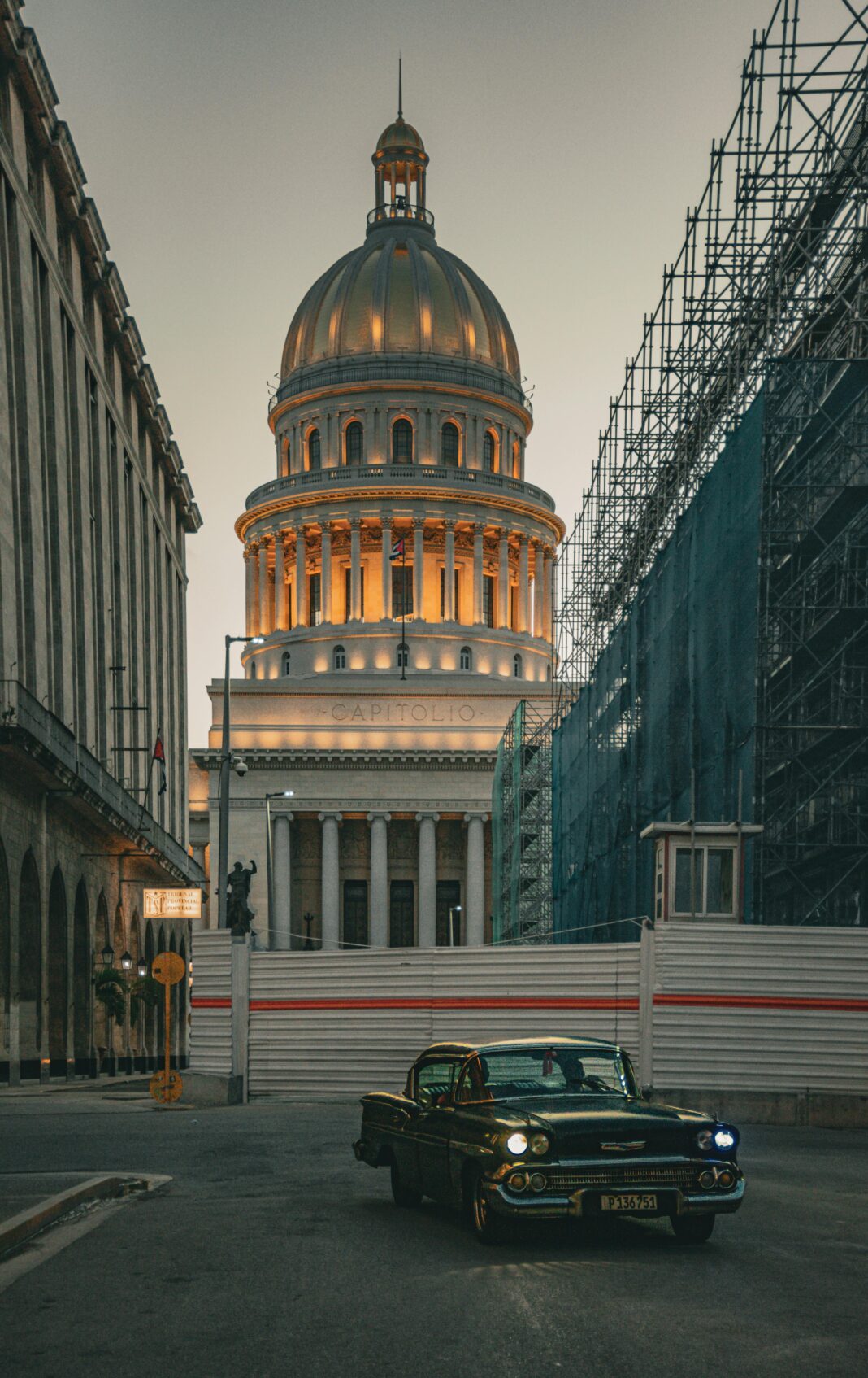 Klasyczny zabytkowy samochód przed El Capitolio w Hawanie o zmierzchu z rusztowaniami na ulicy.