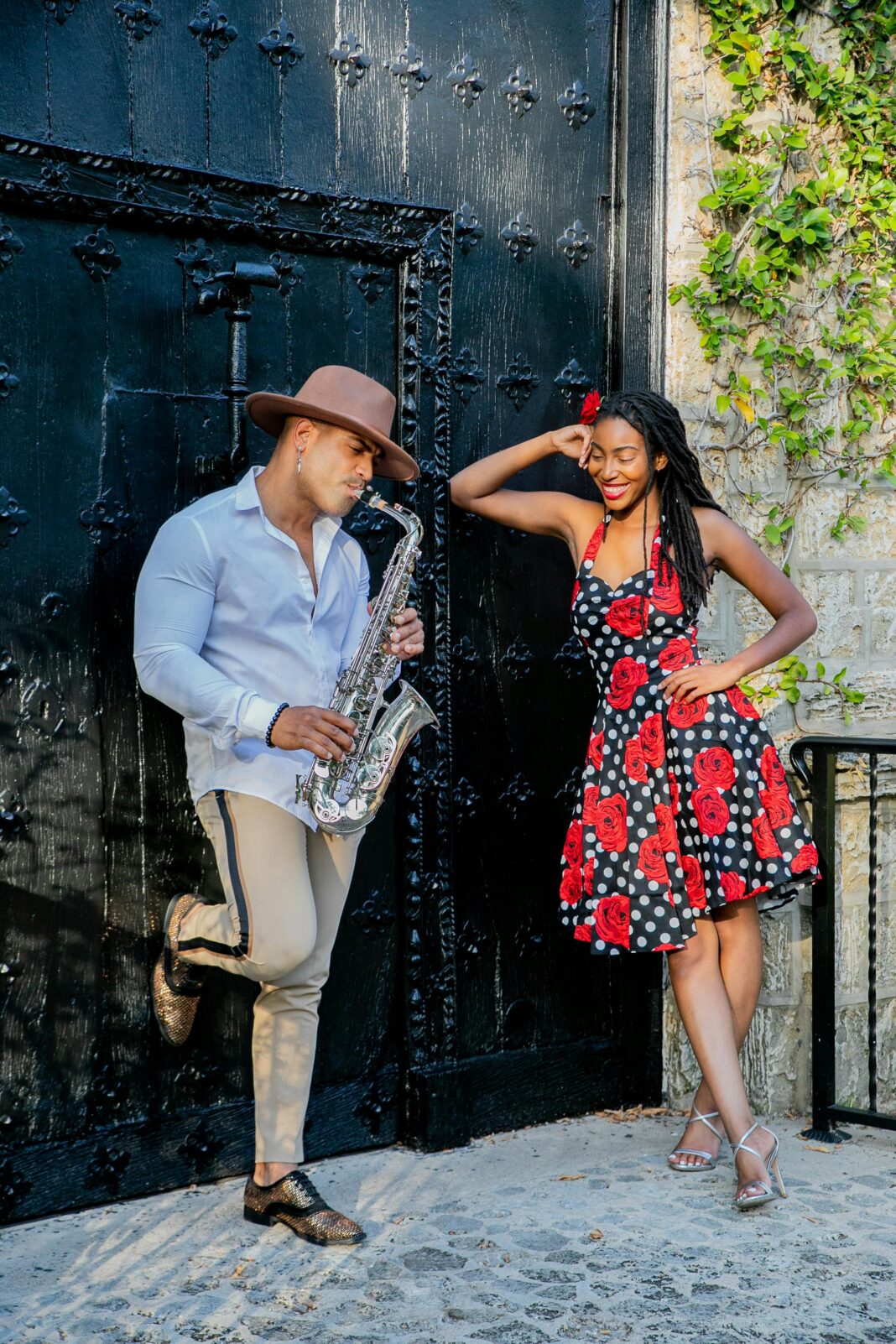 Modny mężczyzna i kobieta pozują z saksofonem na zewnątrz ozdobną czarną bramą.