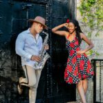 Modny mężczyzna i kobieta pozują z saksofonem na zewnątrz ozdobną czarną bramą.