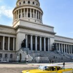 Klasyczny żółty samochód przejeżdżający obok El Capitolio w Hawanie na Kubie, z czystym błękitnym niebem.