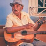 Religia i wierzenia na Kubie – katolicyzm i santeria Starszy gitarzysta występuje na świeżym powietrzu, uosabiając tętniącą życiem kubańską scenę muzyki ulicznej.