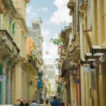 Flaga i symbole narodowe Kuby – znaczenie i historia Turyści spacerujący wąskim deptakiem pomiędzy starymi klasycznymi budynkami w historycznej dzielnicy Hawany w słoneczny letni dzień