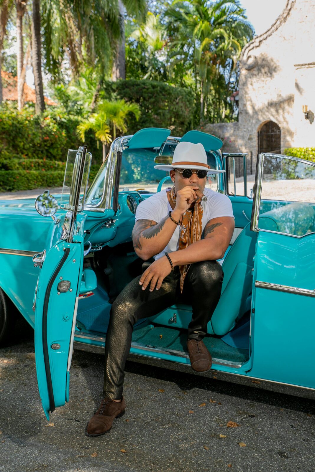 Mężczyzna palący cygaro w zabytkowym kabriolecie pośród kubańskiej scenerii. 