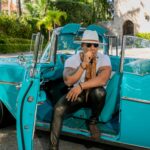 Mężczyzna palący cygaro w zabytkowym kabriolecie pośród kubańskiej scenerii. 