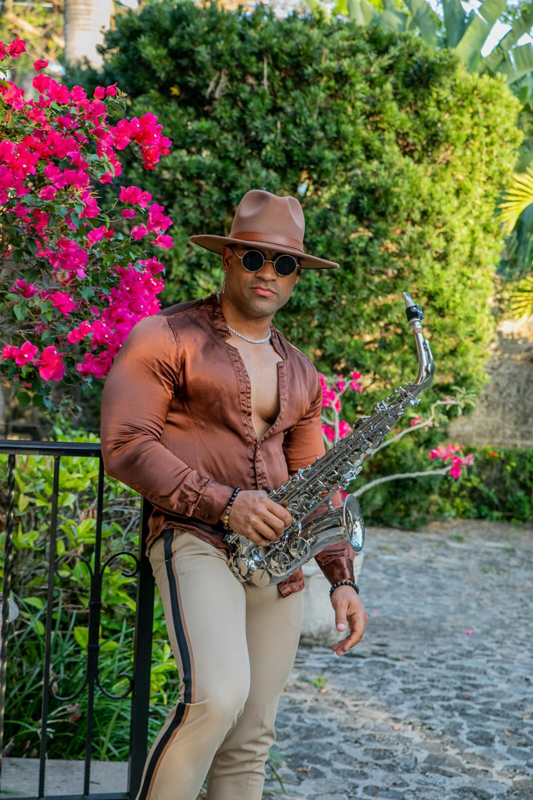 cuba Muskularny saksofonista w satynowej koszuli i kapeluszu pozuje na świeżym powietrzu z kwiatami w Hawanie.