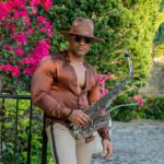 Muskularny saksofonista w satynowej koszuli i kapeluszu pozuje na świeżym powietrzu z kwiatami w Hawanie.