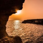 Archeologiczne skarby Cypru: Przegląd najważniejszych stanowisk archeologicznych Zapierający dech w piersiach zachód słońca nad oceanem oglądany z jaskini morskiej na Cyprze, tworząc spokojny krajobraz morski.