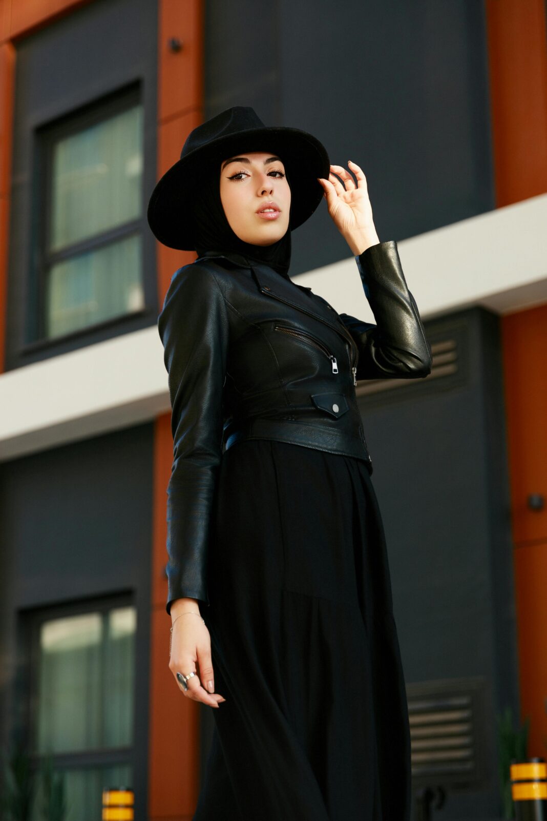 cypr Modna kobieta w czarnym stroju i kapeluszu pewnie pozuje na świeżym powietrzu w miejskim otoczeniu, prezentując nowoczesny styl.