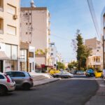 Cypr dla Rodzin: Atrakcje dla Najmłodszych i Wskazówki dla Rodziców Nasłoneczniona ulica w śródziemnomorskim mieście z samochodami i nowoczesną architekturą.