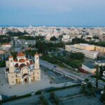 Cypr Nocą: Przegląd Najlepszych Klubów i Barów Ujęcie drona kościoła św. Jerzego Kontosa w Larnace na Cyprze, na tle pejzażu miejskiego.