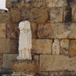 Wina cypryjskie: Historia winiarstwa na Cyprze Starożytny posąg w Kıbrıs stoi pod historycznym kamiennym murem.