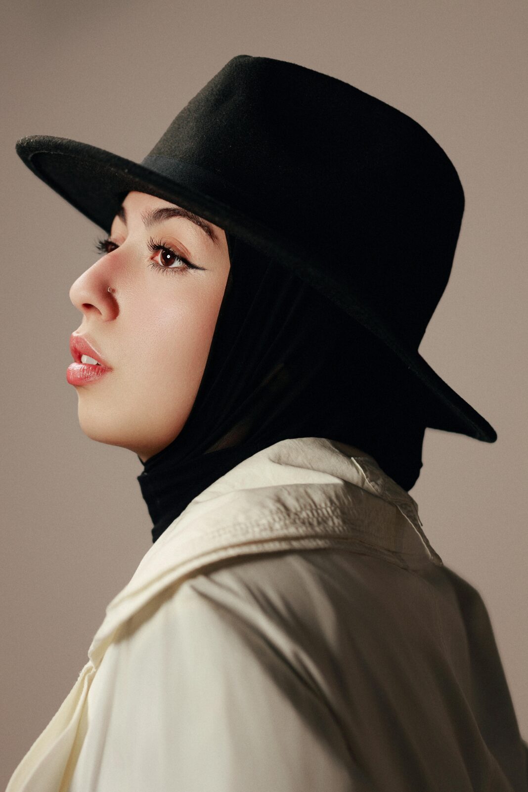 Profil boczny kobiety w hidżabie i fedorze, ukazujący elegancję i różnorodność.