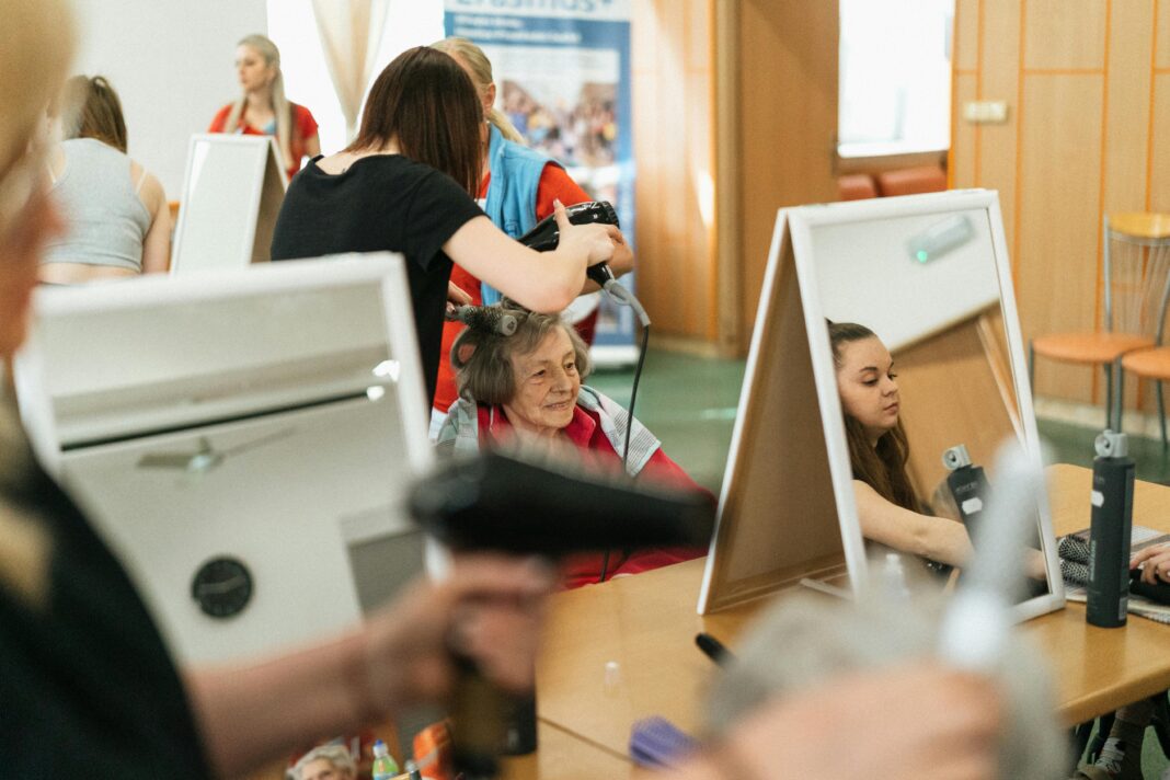 Starsza kobieta uśmiecha się podczas sesji stylizacyjnej w tętniącym życiem salonie fryzjerskim w Karwinie.