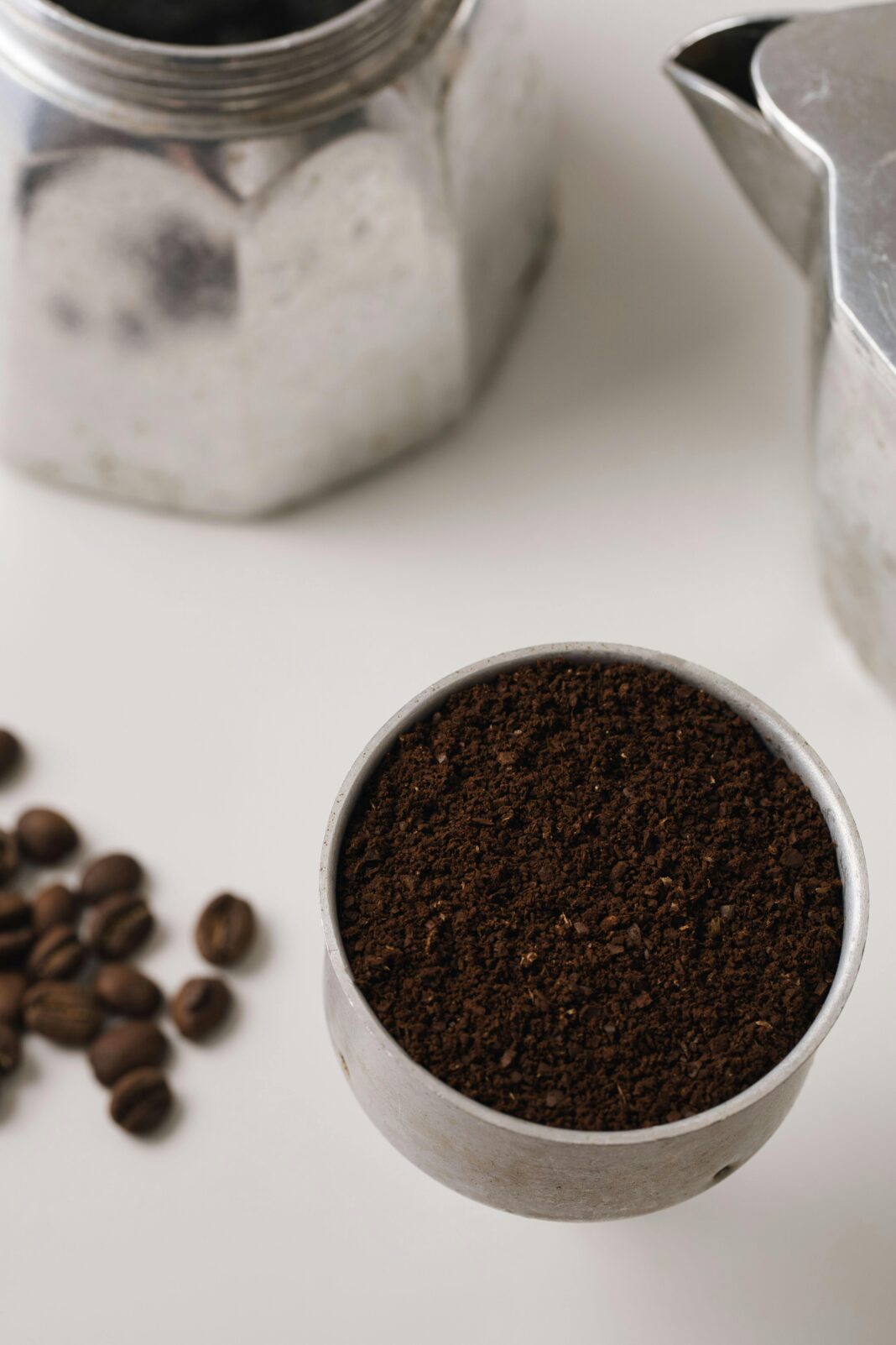 Zbliżenie mielonej kawy i dzbanka do moki na białej powierzchni, idealne do motywów kawiarnianych lub kuchennych.