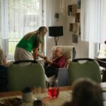 Opiekun pomagający starszym kobietom w piciu herbaty w przytulnym domu opieki.