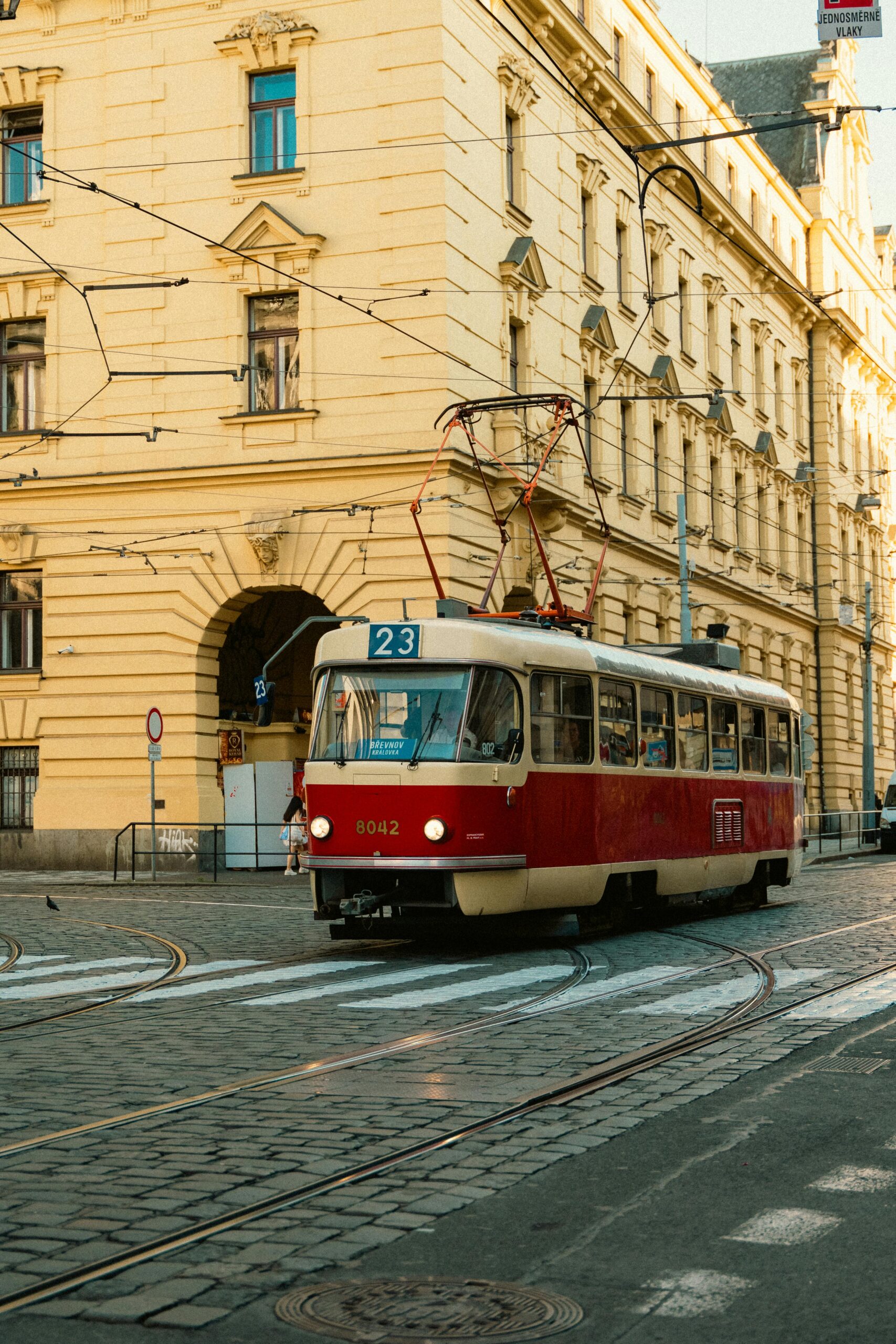Klasyczny czerwony tramwaj na historycznej brukowanej uliczce w malowniczym miejskim otoczeniu Pragi.