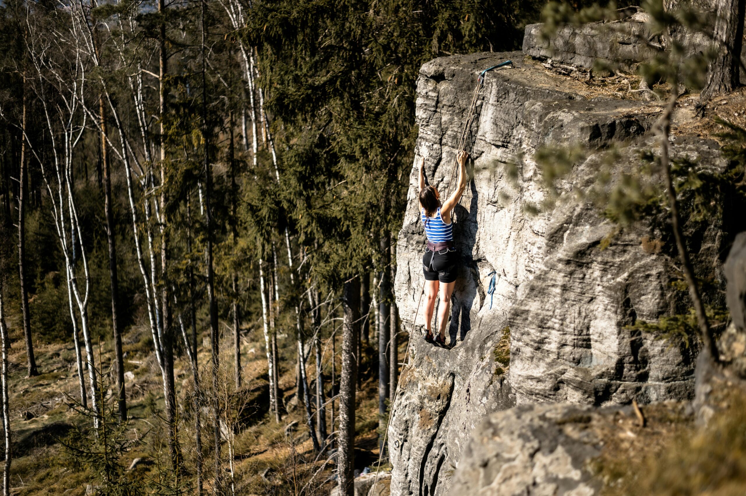 Kobieta wspinająca się po skalnej ścianie otoczonej bujnym lasem w Trutnovie w Czechach.