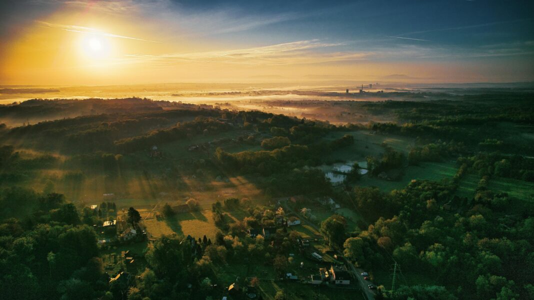 Zapierający dech w piersiach widok z lotu ptaka na okolicę Orłową o wschodzie słońca, ukazujący bujne zielone wzgórza i tętniący życiem krajobraz.