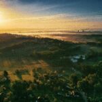 Zamek Buchlov – niezdobyta twierdza Wschodnich Moraw Zapierający dech w piersiach widok z lotu ptaka na okolicę Orłową o wschodzie słońca, ukazujący bujne zielone wzgórza i tętniący życiem krajobraz.