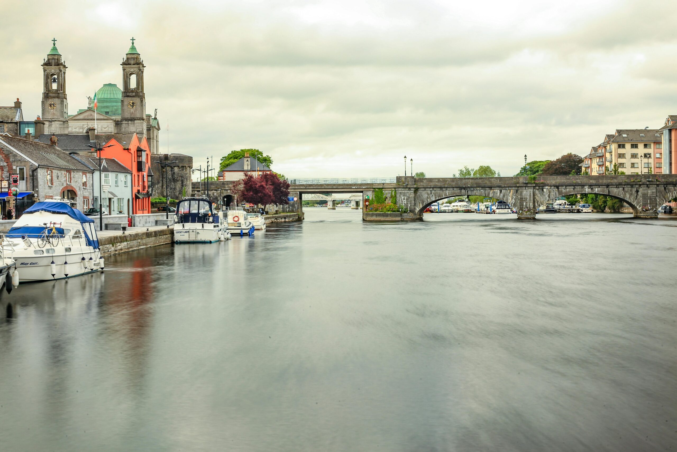 Malownicza scena mostu Athlone nad spokojną rzeką w Irlandii z łodziami i zabytkowymi budynkami.