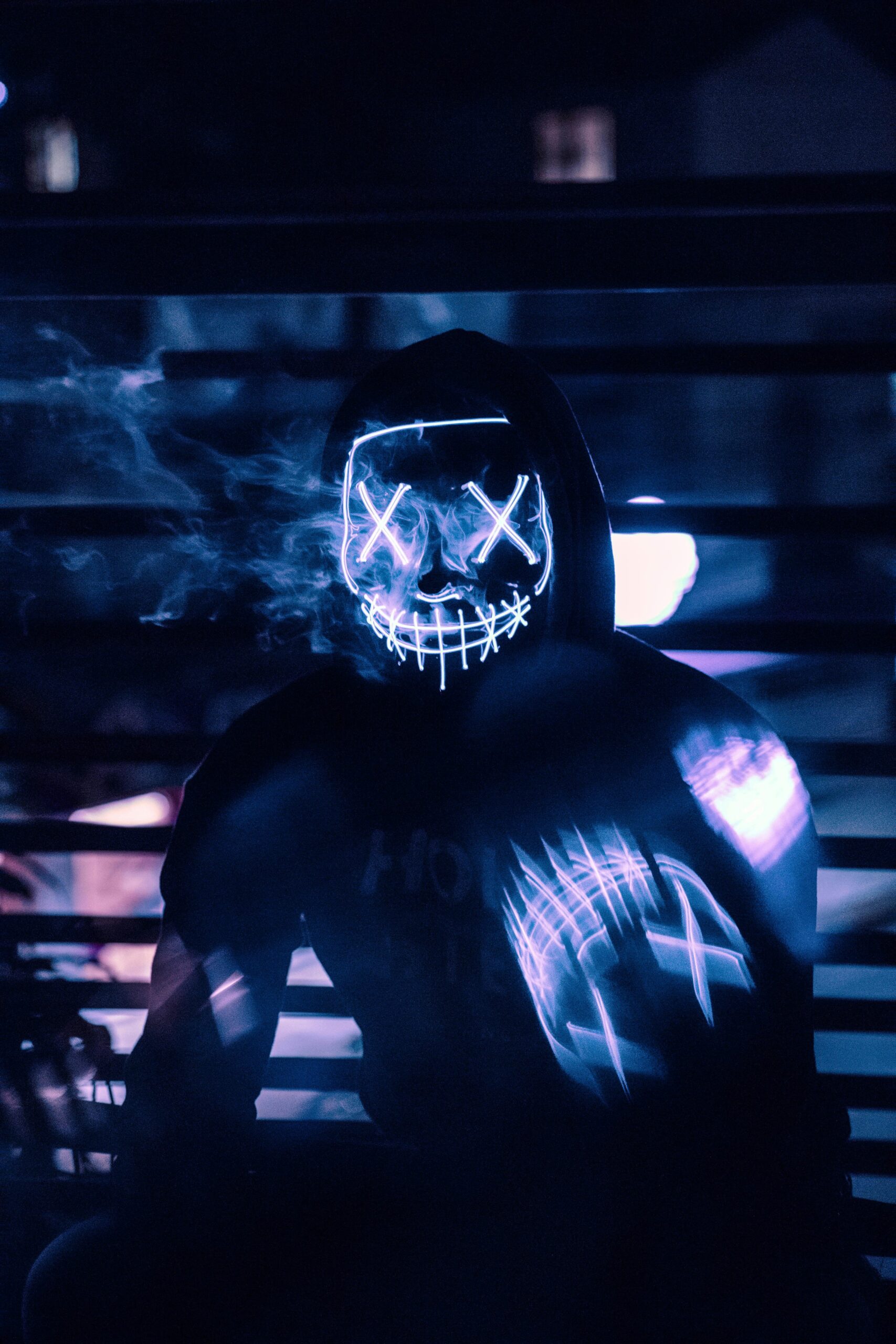 Tajemnicza postać w neonowej masce i bluzie uchwycona nocą, emanująca enigmatyczną atmosferą.