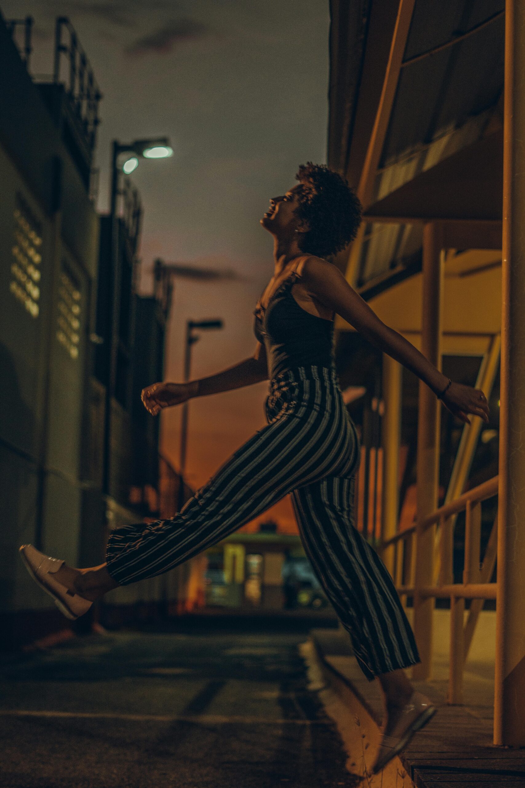 Stylowa kobieta pozuje twórczo w ciemnej, miejskiej uliczce, ubrana w spodnie w paski.