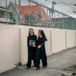 Degustacja cygar w Dominikanie – gdzie i jak spróbować? Dwie zakonnice spacerują i wesoło rozmawiają wzdłuż płotu w pochmurny dzień.