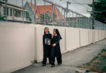 Dwie zakonnice spacerują i wesoło rozmawiają wzdłuż płotu w pochmurny dzień.