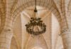 Okazały żyrandol zwisający z kamiennych łuków w starej katedrze, przedstawiający architekturę gotycką.