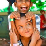 Dwóch uśmiechniętych chłopców bawiących się na świeżym powietrzu na Dominikanie, cieszących się letnimi klimatami.