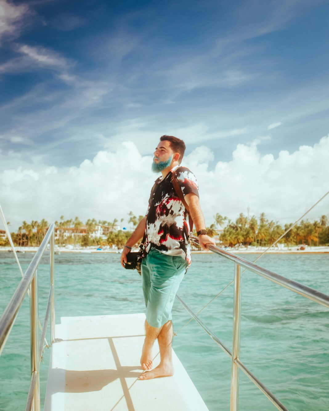 Mężczyzna stojący na pokładzie łodzi, cieszący się słonecznym widokiem na ocean z palmami w tle.