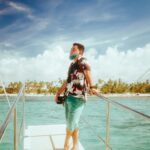 Mężczyzna stojący na pokładzie łodzi, cieszący się słonecznym widokiem na ocean z palmami w tle.