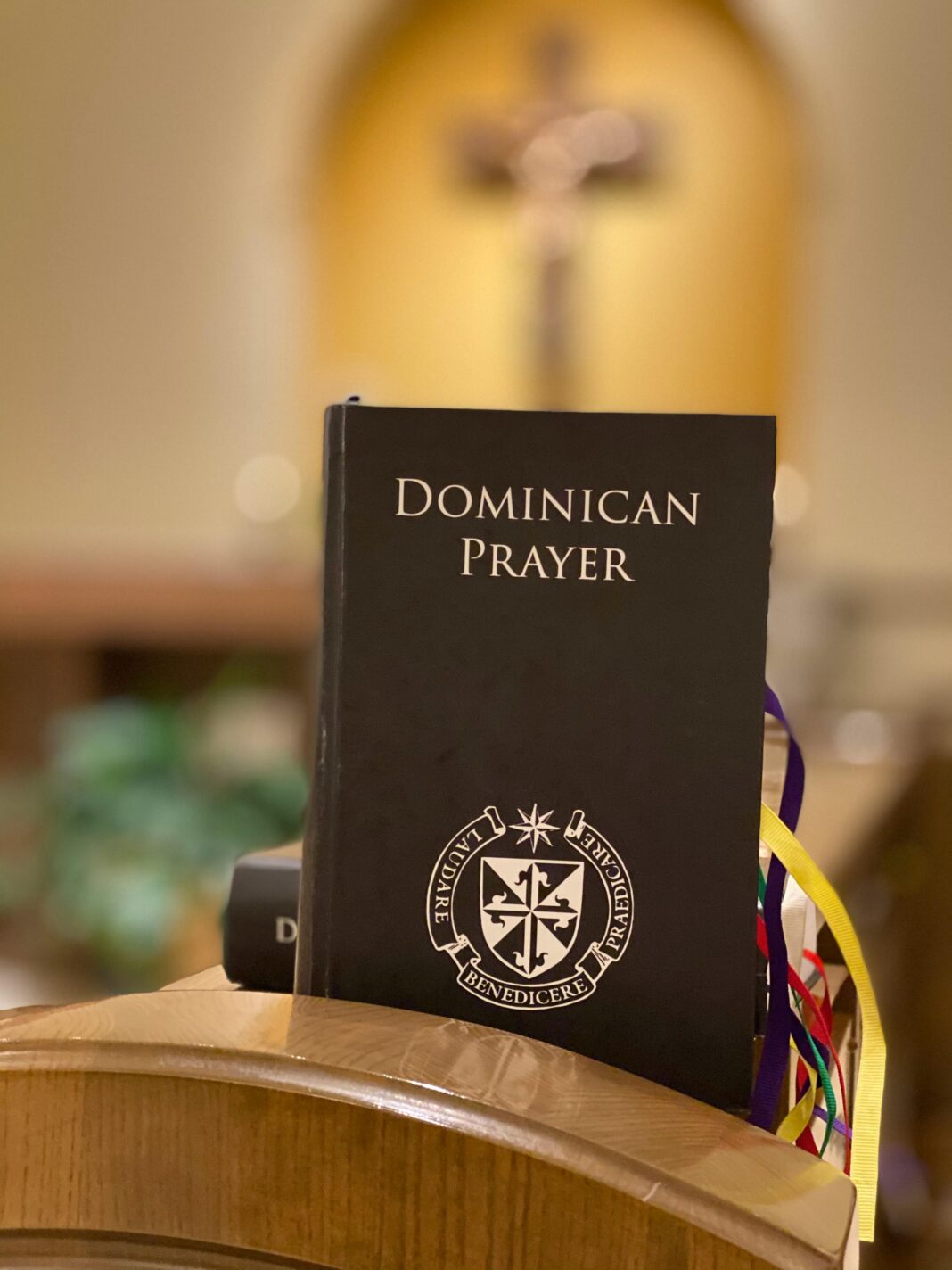 Modlitewnik dominikański na drewnianym stojaku, w tle rozmazany krzyż.
