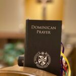 Modlitewnik dominikański na drewnianym stojaku, w tle rozmazany krzyż.