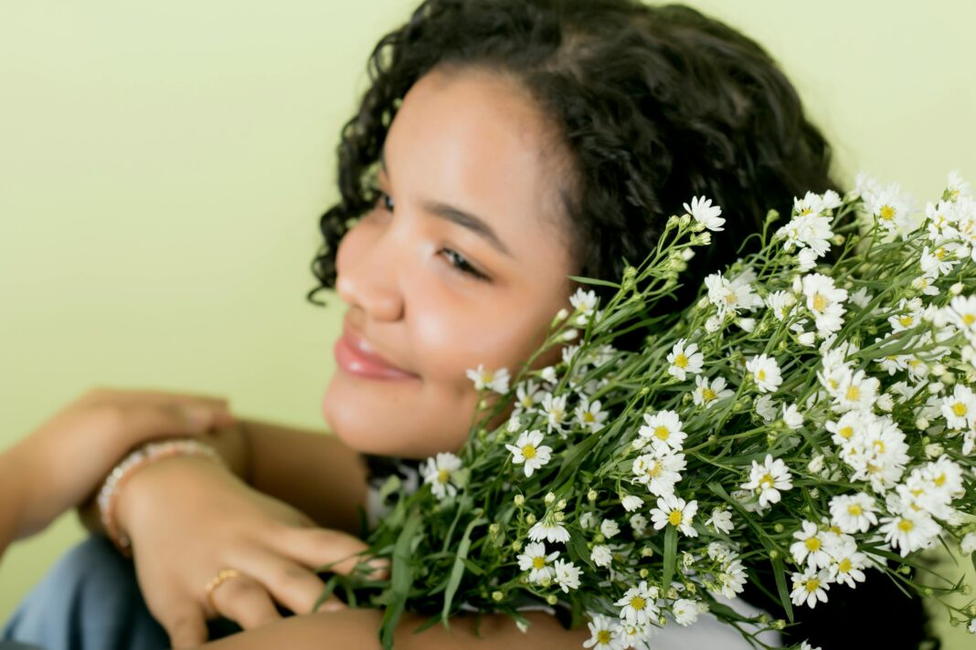 Portret uśmiechniętej kobiety ze stokrotkami, uchwycony w studiu na delikatnym, jasnym tle.