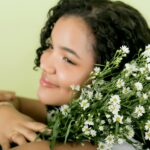 Portret uśmiechniętej kobiety ze stokrotkami, uchwycony w studiu na delikatnym, jasnym tle.