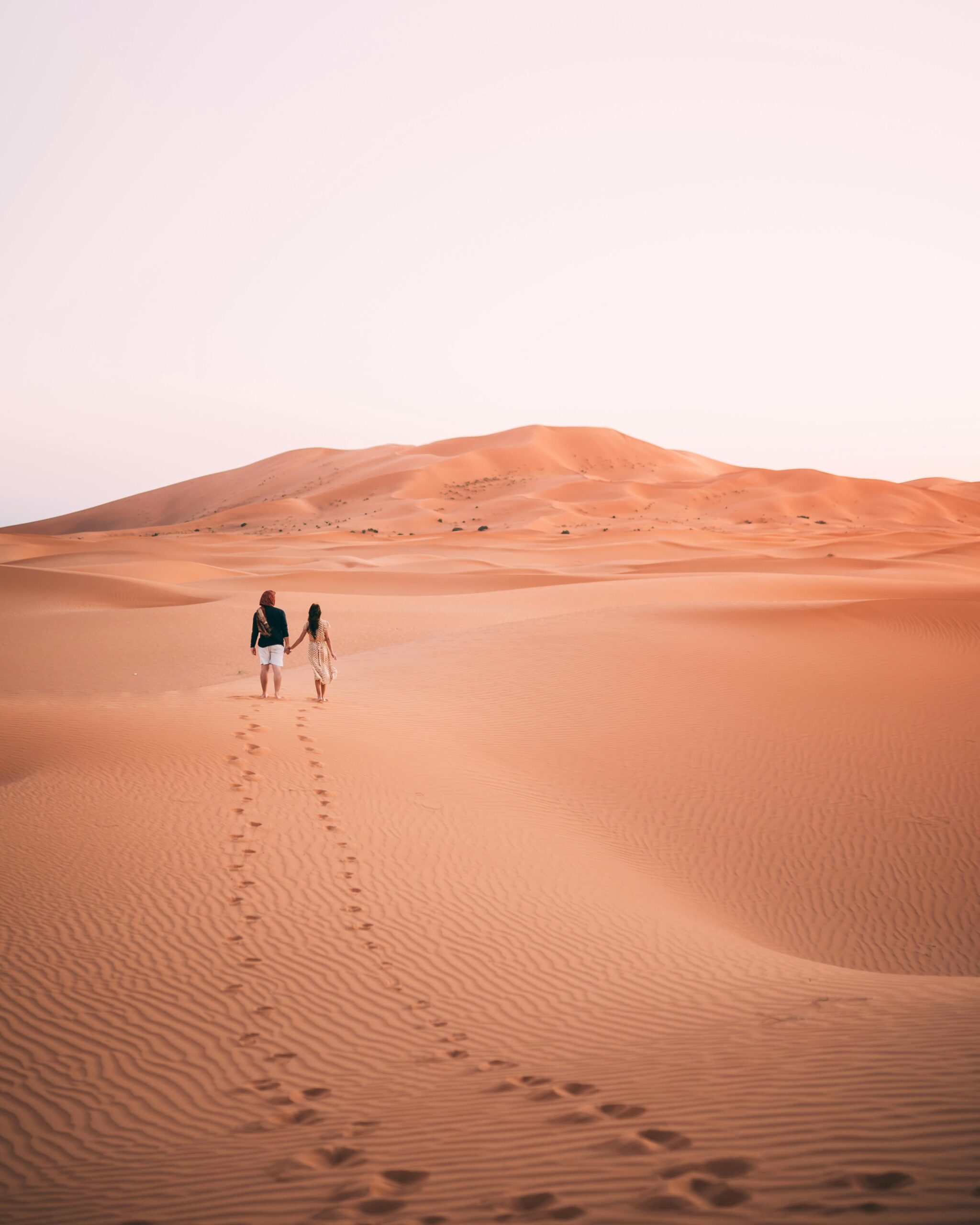 Para spacerująca ramię w ramię przez wydmy na pustyni Al Wahat Al Dakhla o wschodzie słońca.