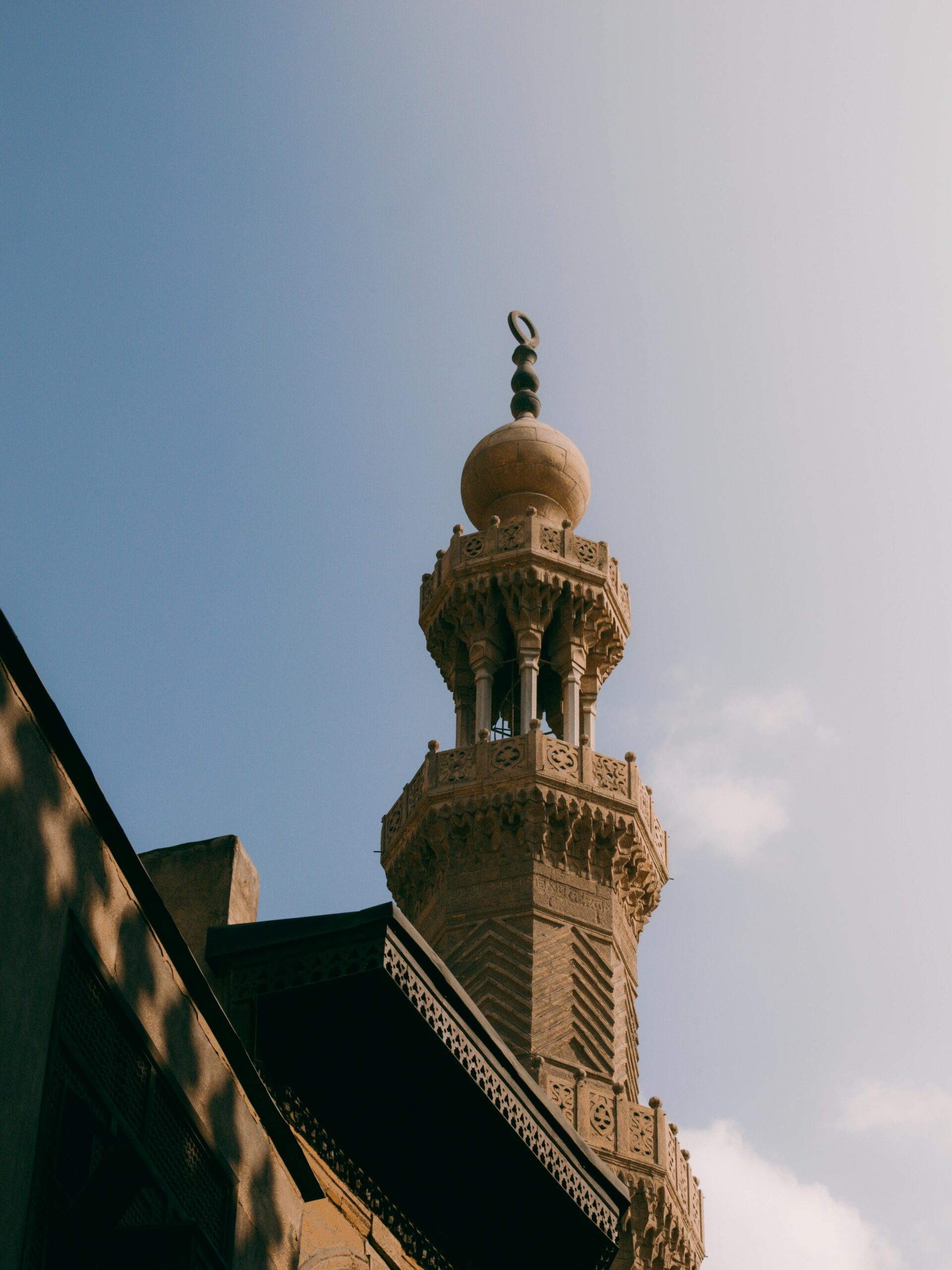 Pięknie szczegółowy minaret meczetu pod czystym błękitnym niebem, przedstawiający architekturę islamską.