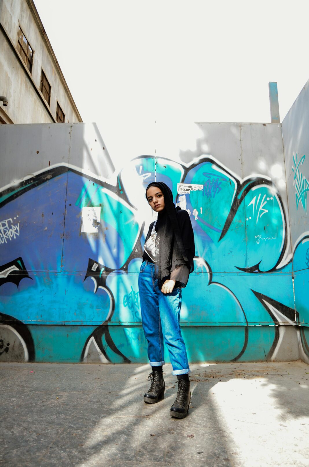 egipt Stylowa kobieta stojąca pewnie przed tętniącą życiem ścianą graffiti w Kairze.