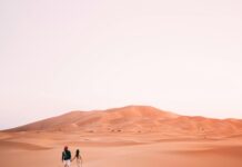 Para spacerująca ramię w ramię przez wydmy na pustyni Al Wahat Al Dakhla o wschodzie słońca.