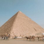 Ludzie z końmi spacerujący w pobliżu piramidy Cheopsa, największej egipskiej piramidy, pomnika sztuki architektonicznej starożytnego Egiptu