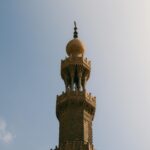 Wysoki, ozdobny minaret wznoszący się na tle czystego nieba, symbolizujący historyczną architekturę islamską.