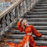 Stylowa kobieta pozowała na kamiennych schodach w stylu vintage w pomarańczowej sukience, oddając jesienne klimaty.