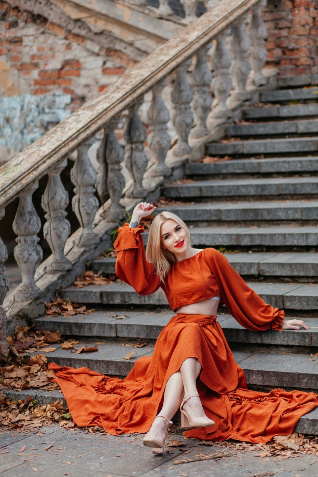 Stylowa kobieta pozowała na kamiennych schodach w stylu vintage w pomarańczowej sukience, oddając jesienne klimaty.