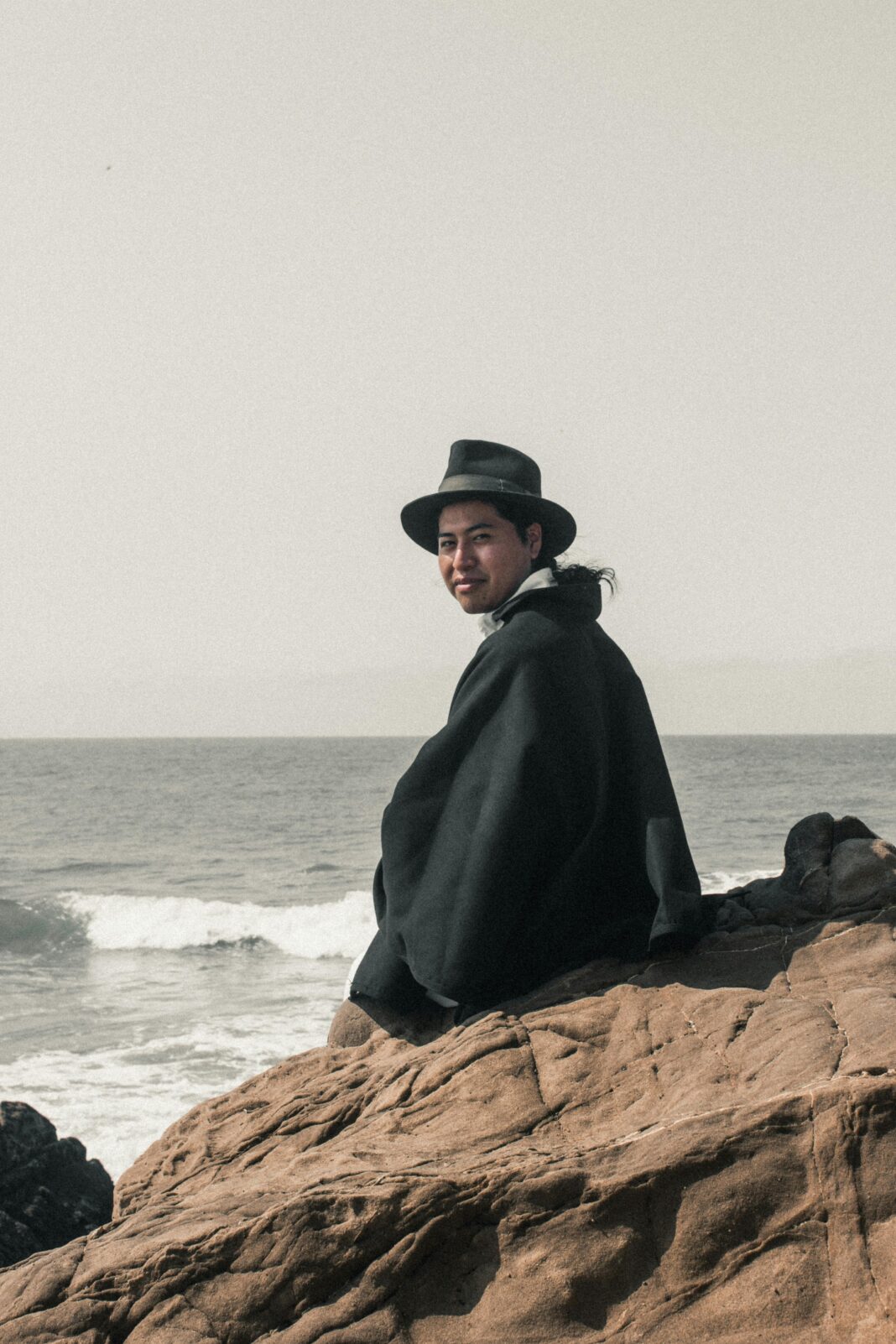 ekwador Młody mężczyzna w kapeluszu i płaszczu siedzi na skalistym wybrzeżu w Engabao w Ekwadorze.