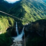 Piękny wodospad spływający kaskadą przez bujne zielone wzgórza pod jasnym niebem, ukazujący spokojne piękno natury.