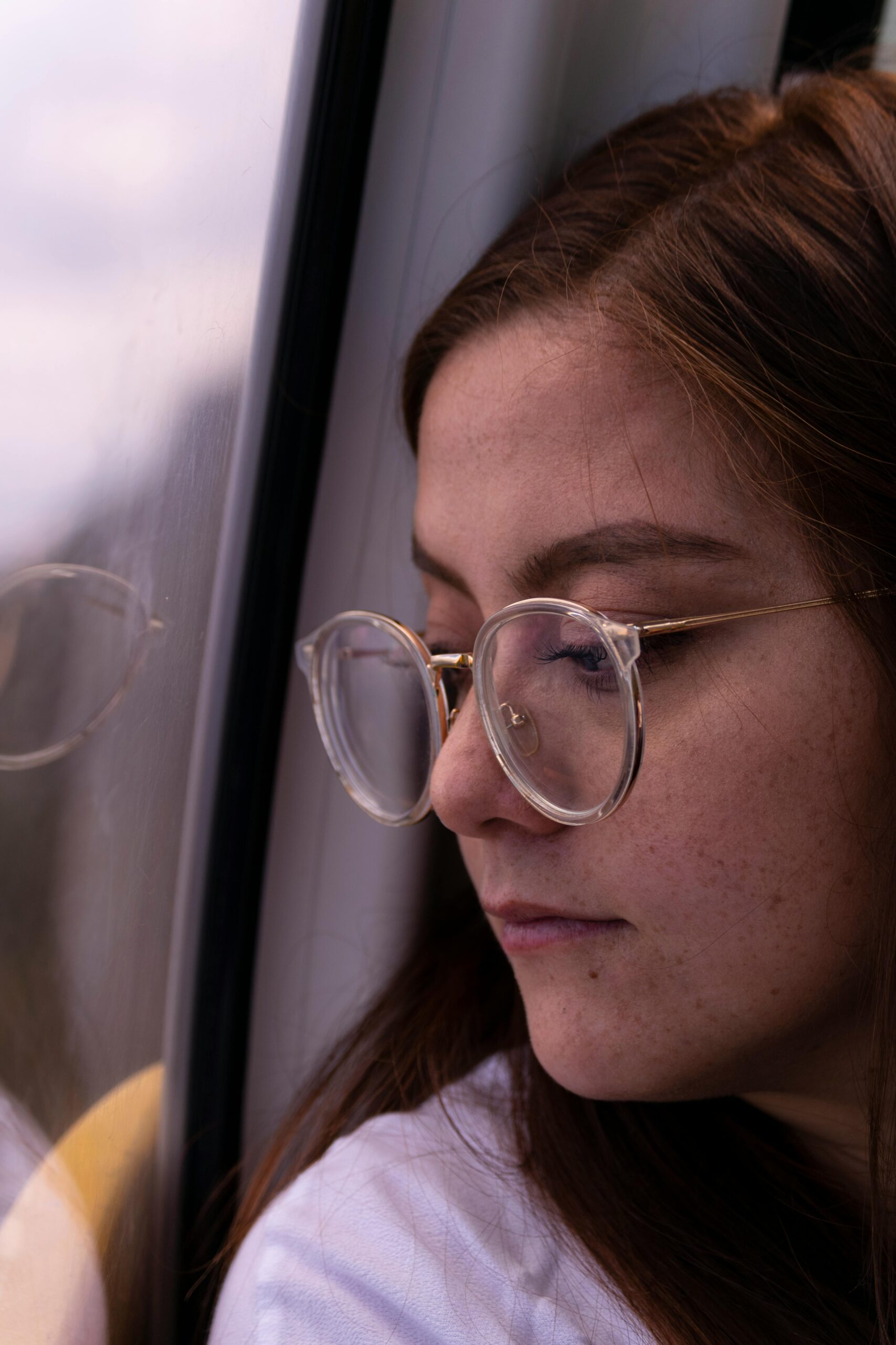 Spokojny portret kobiety w okularach, w zamyśleniu odbijającej się w oknie.