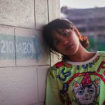 Portret młodej kobiety opartej o ścianę w miejskim tle, prezentującej kolorową modę na Filipinach.