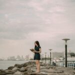 Kobieta czyta na skalistym brzegu Zatoki Manilskiej, na tle panoramy miasta.