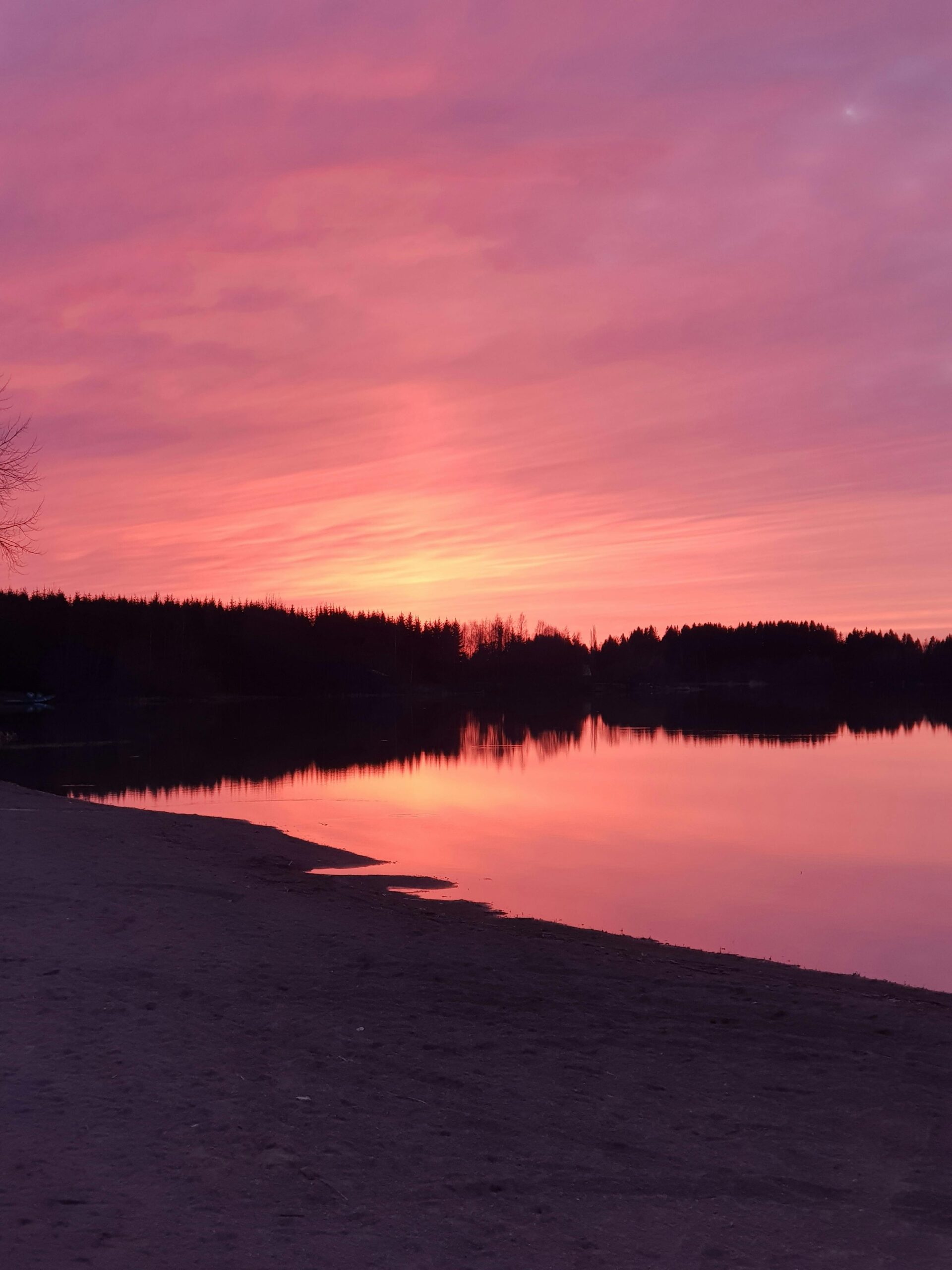 Malowniczy zachód słońca z żywym różowym niebem nad spokojnym jeziorem w Finlandii.